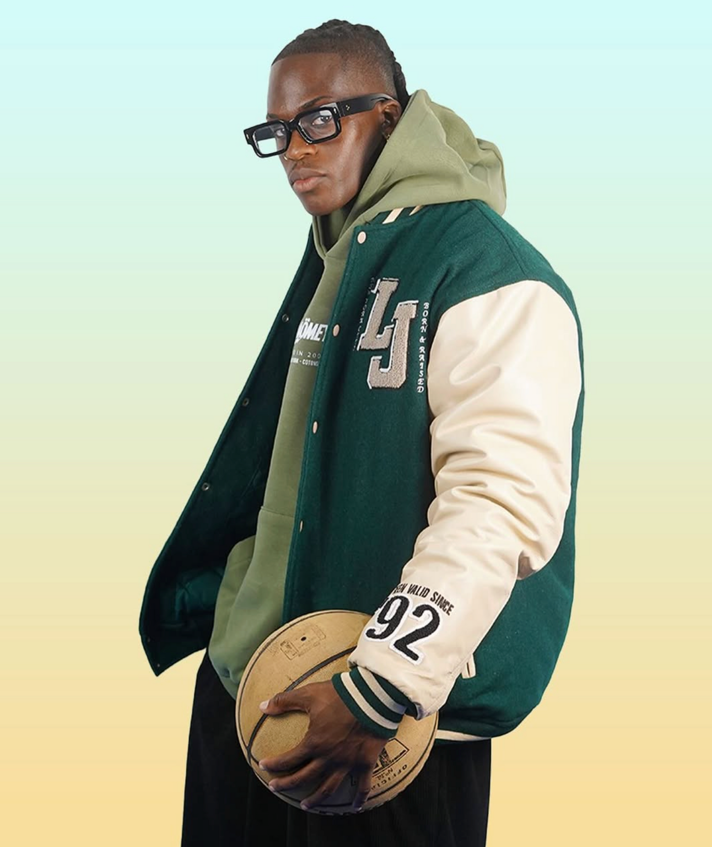 Person wearing a green and beige varsity jacket holding a basketball against a gradient background, featuring the brand DAÖMEY.
