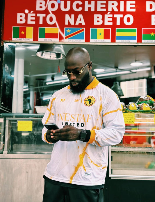 Man wearing West Africa sports jersey by Daömey with a store and flags in the background